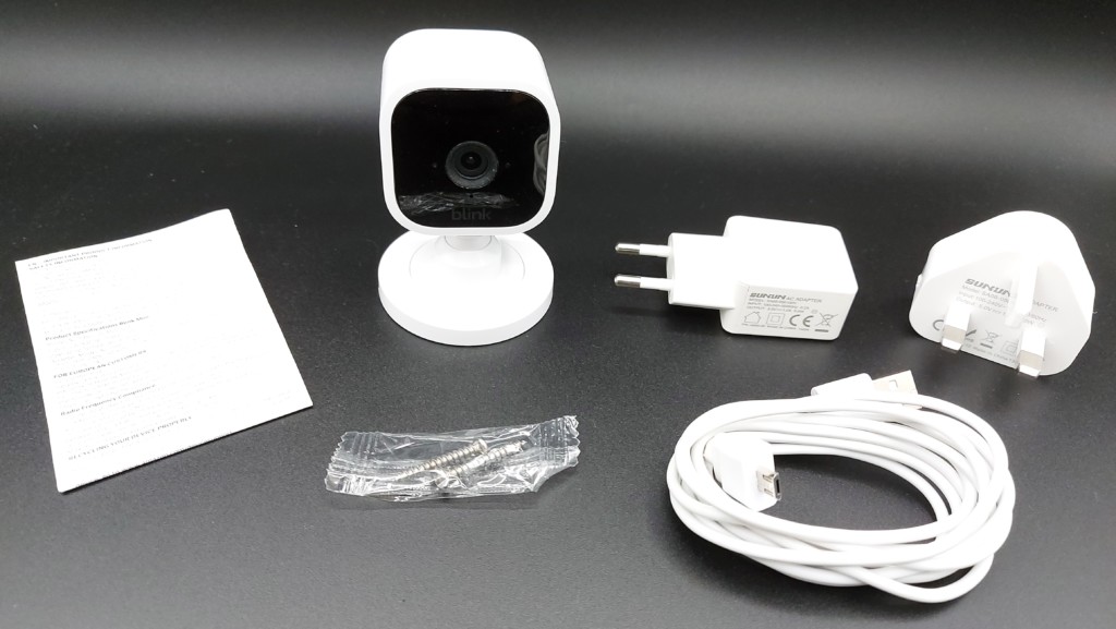 contenu du coffret de la Blink mini caméra : caméra blanche avec support, deux adaptateur UK et EU, cable micro-USB et deux vis